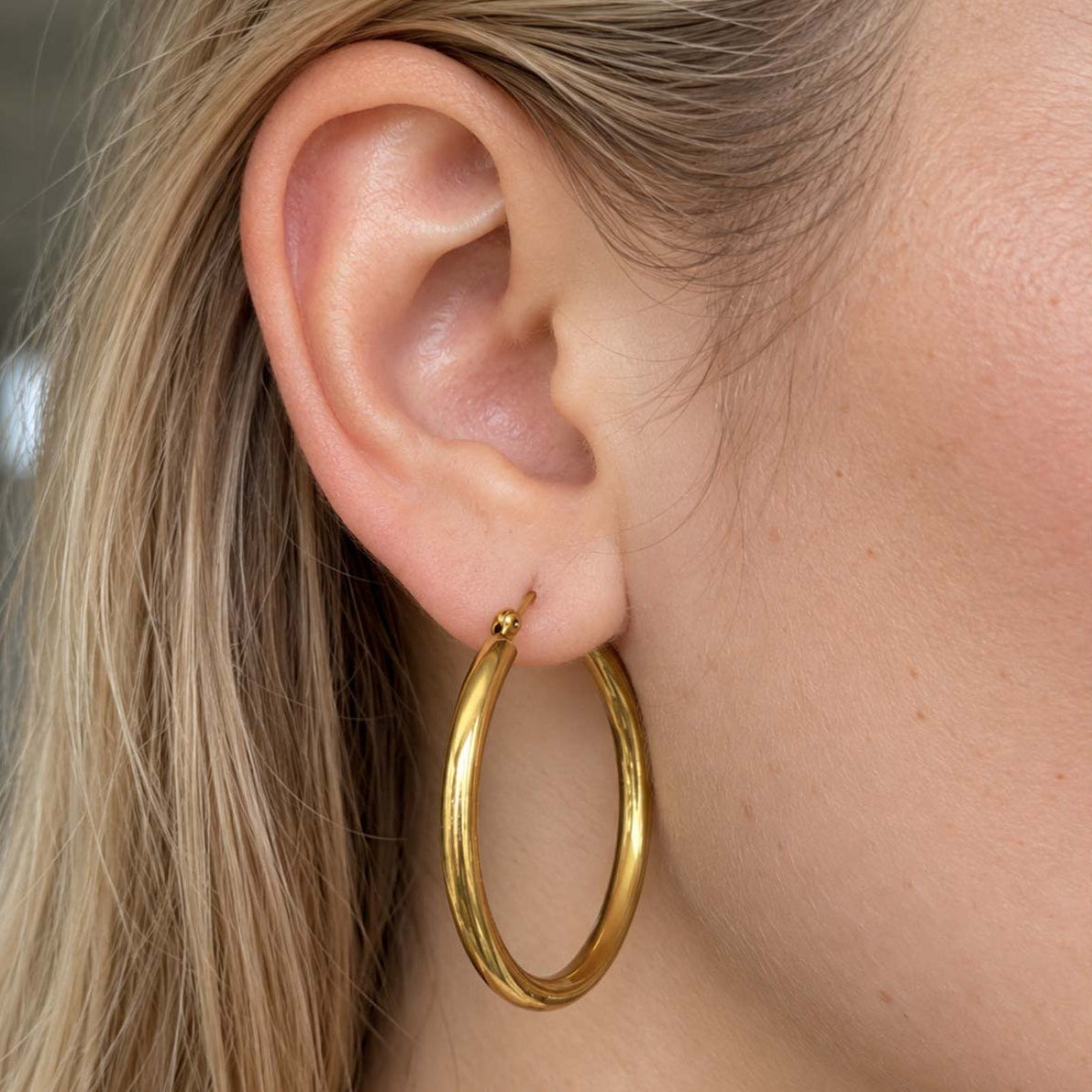 A close-up of a person's ear wearing a polished gold hoop earring.
